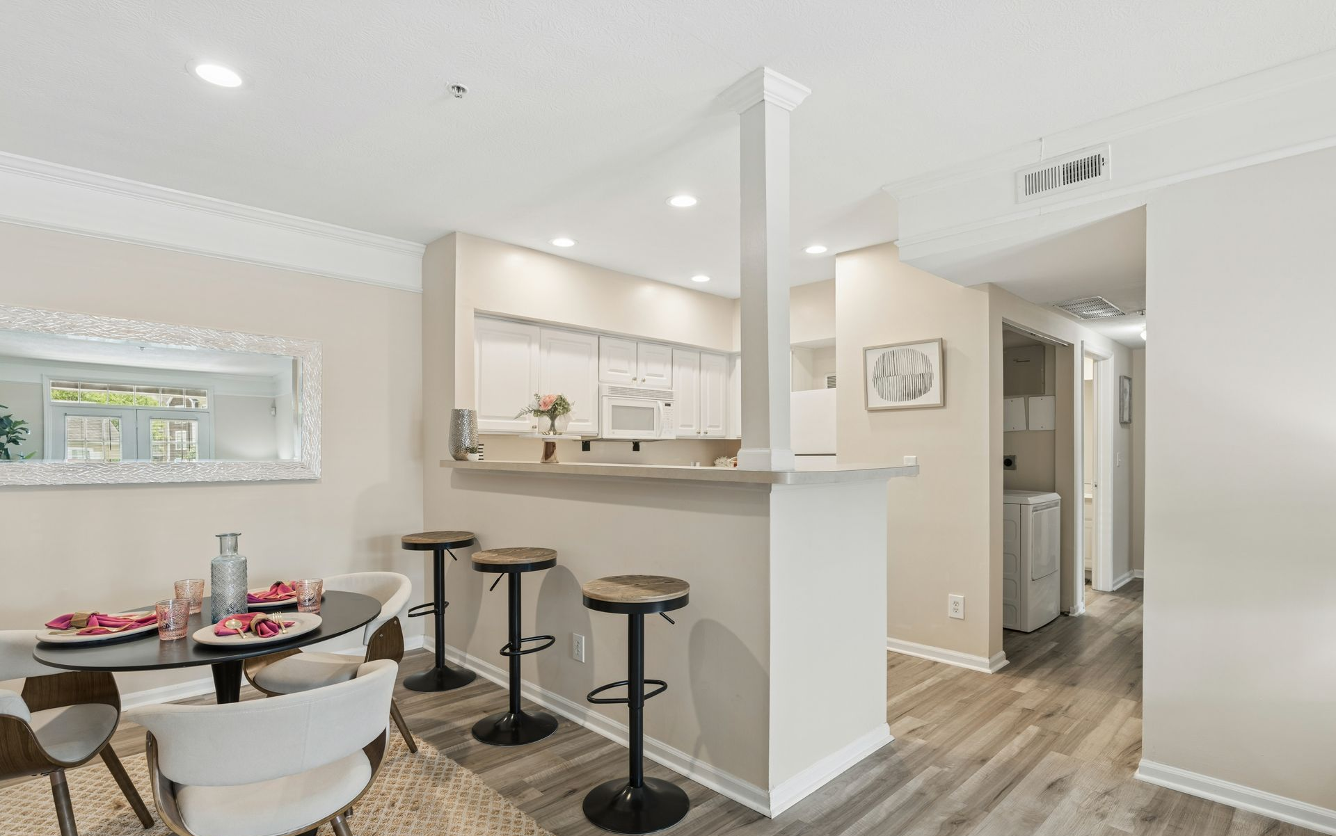 Bright open kitchen and dining area with white walls, bar stools, and wood floors.