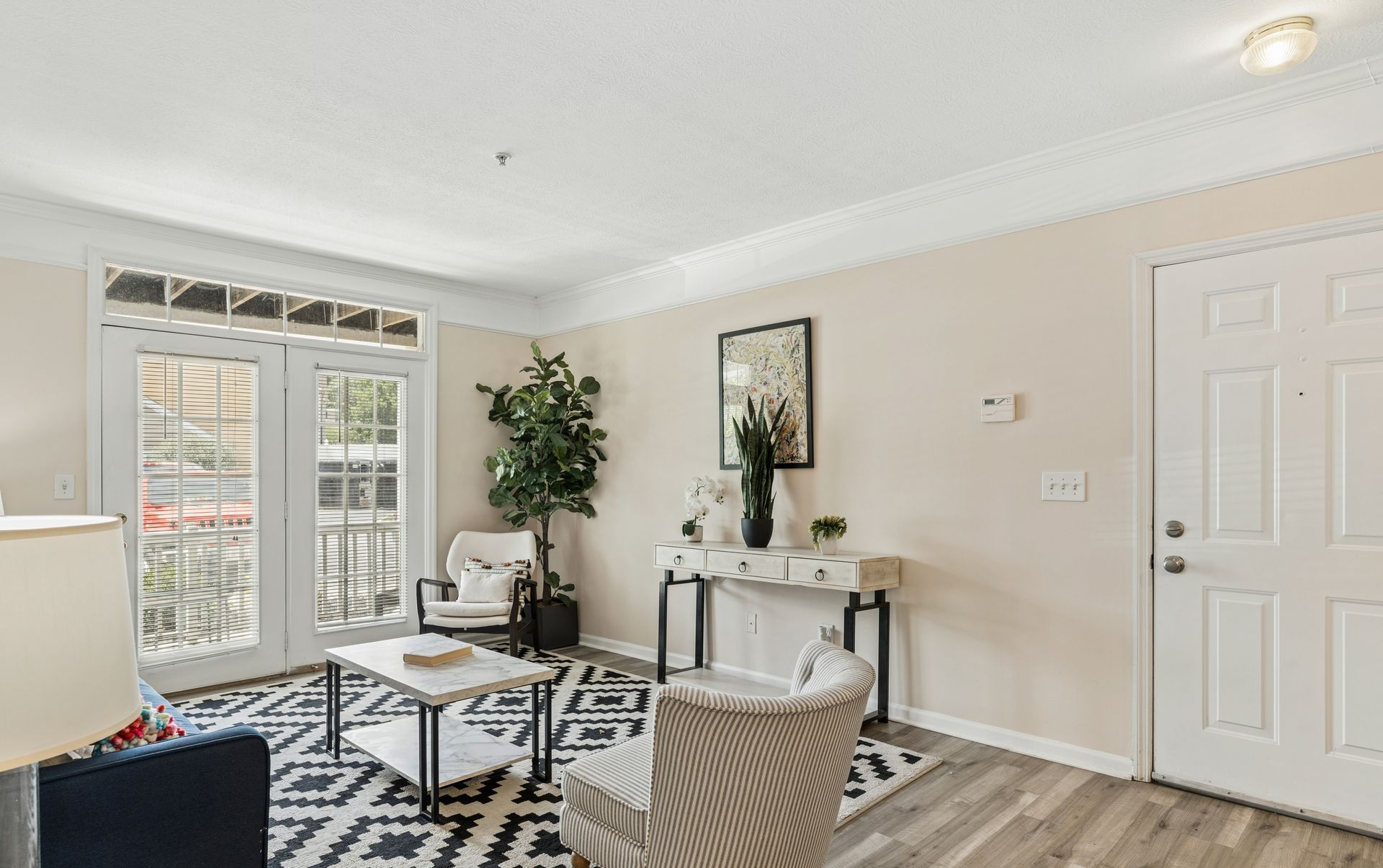 Bright living room with gray sofa, patterned rug, glass coffee table, console table, and white French doors.