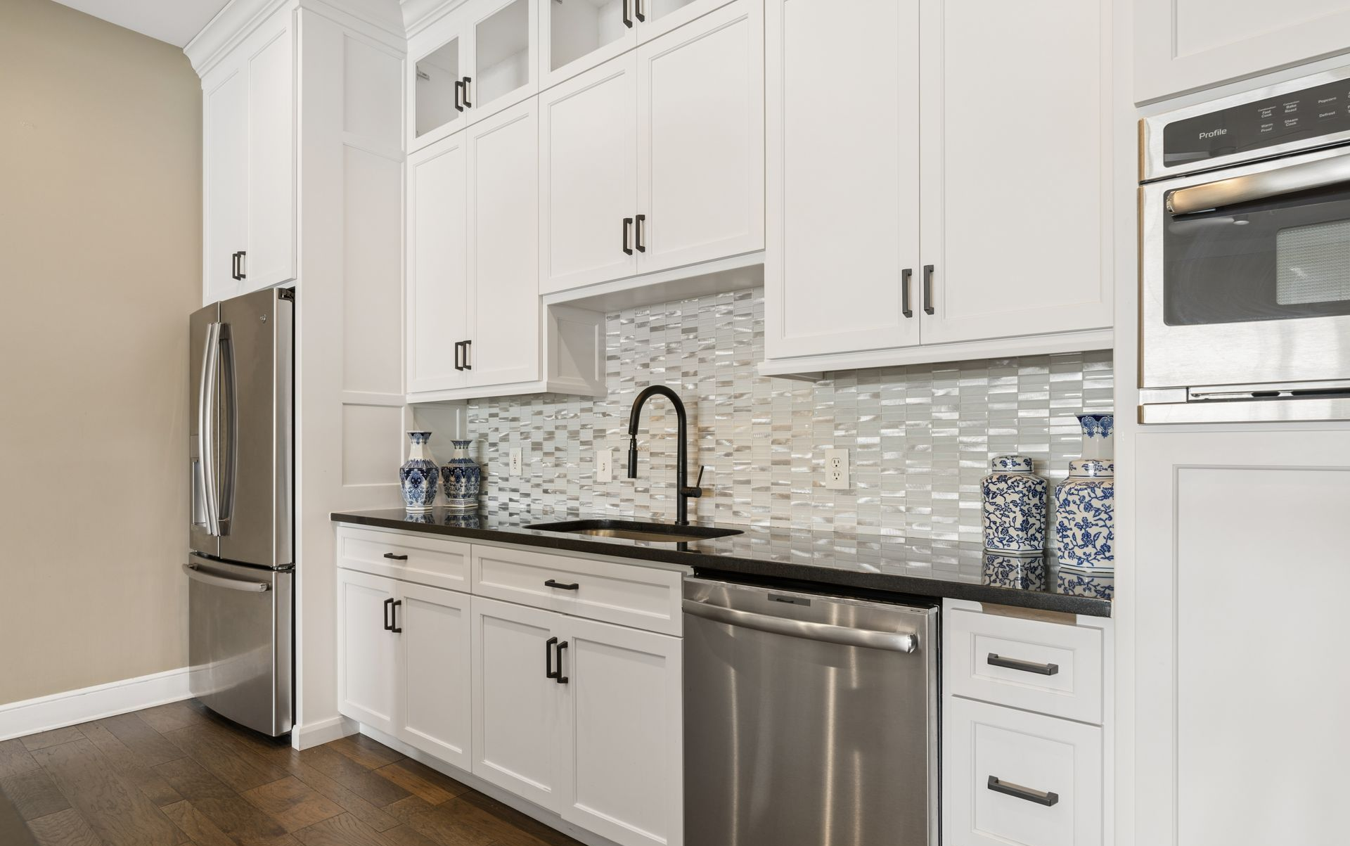 Modern white kitchen with stainless steel appliances, black countertops, and mosaic tile backsplash.