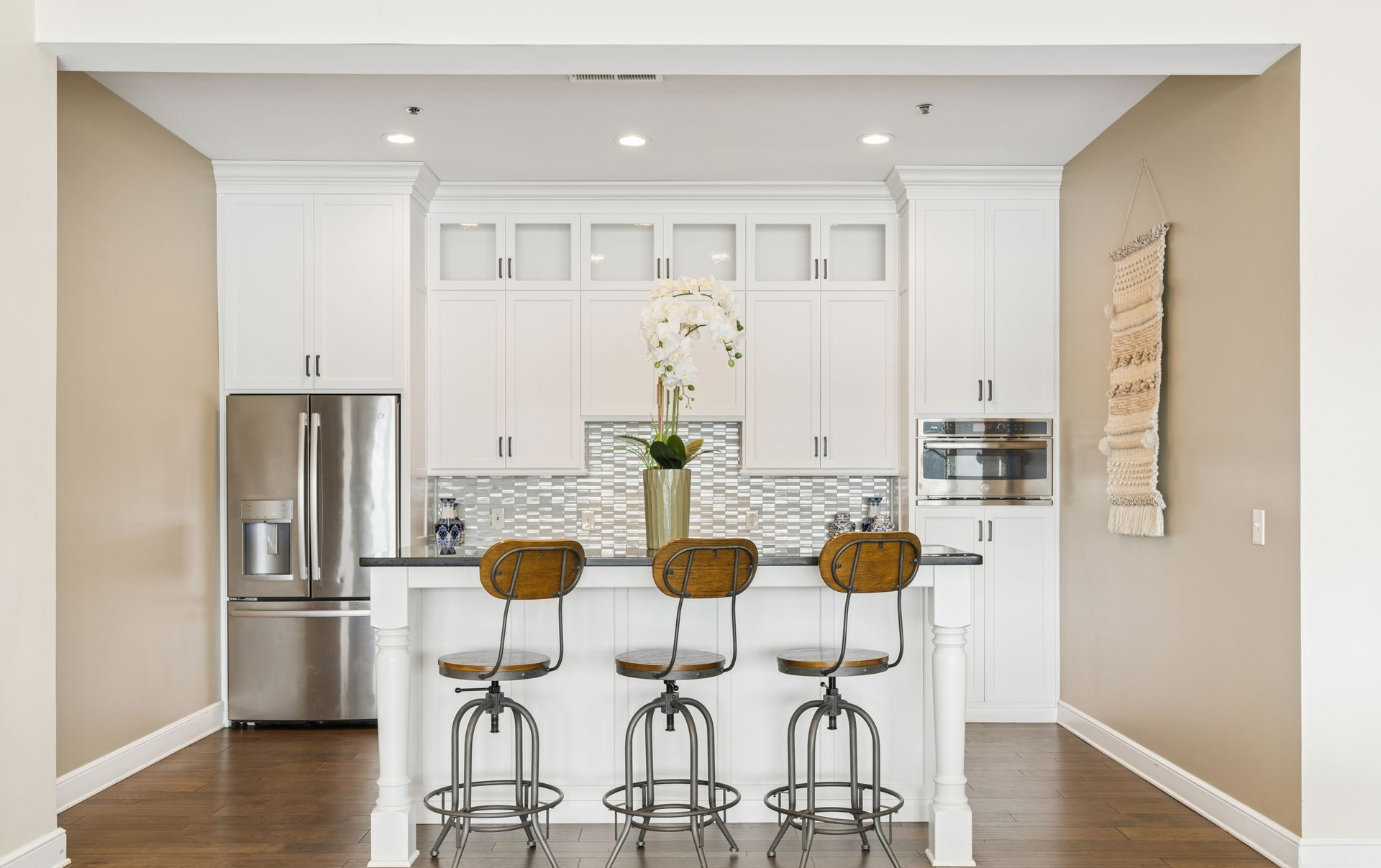 Modern white kitchen with stainless steel appliances, island seating, and hardwood floors.