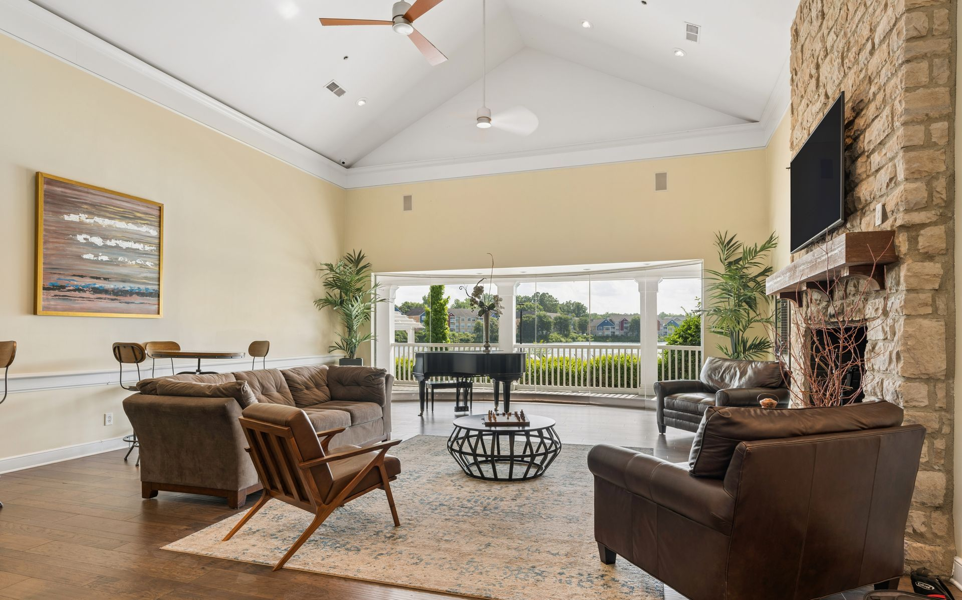Spacious club room with leather chairs, stone fireplace, high ceiling, and open view to a sunlit balcony.