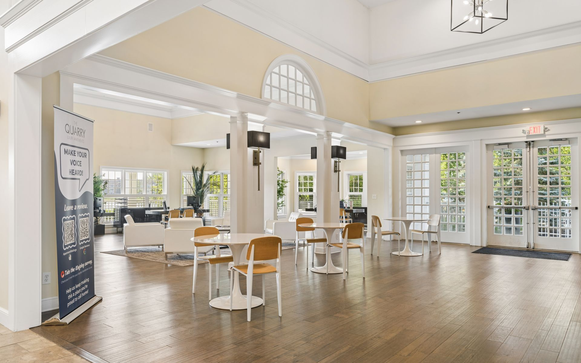 Bright, airy lobby with white columns, wooden floors, and small tables and chairs near glass doors.