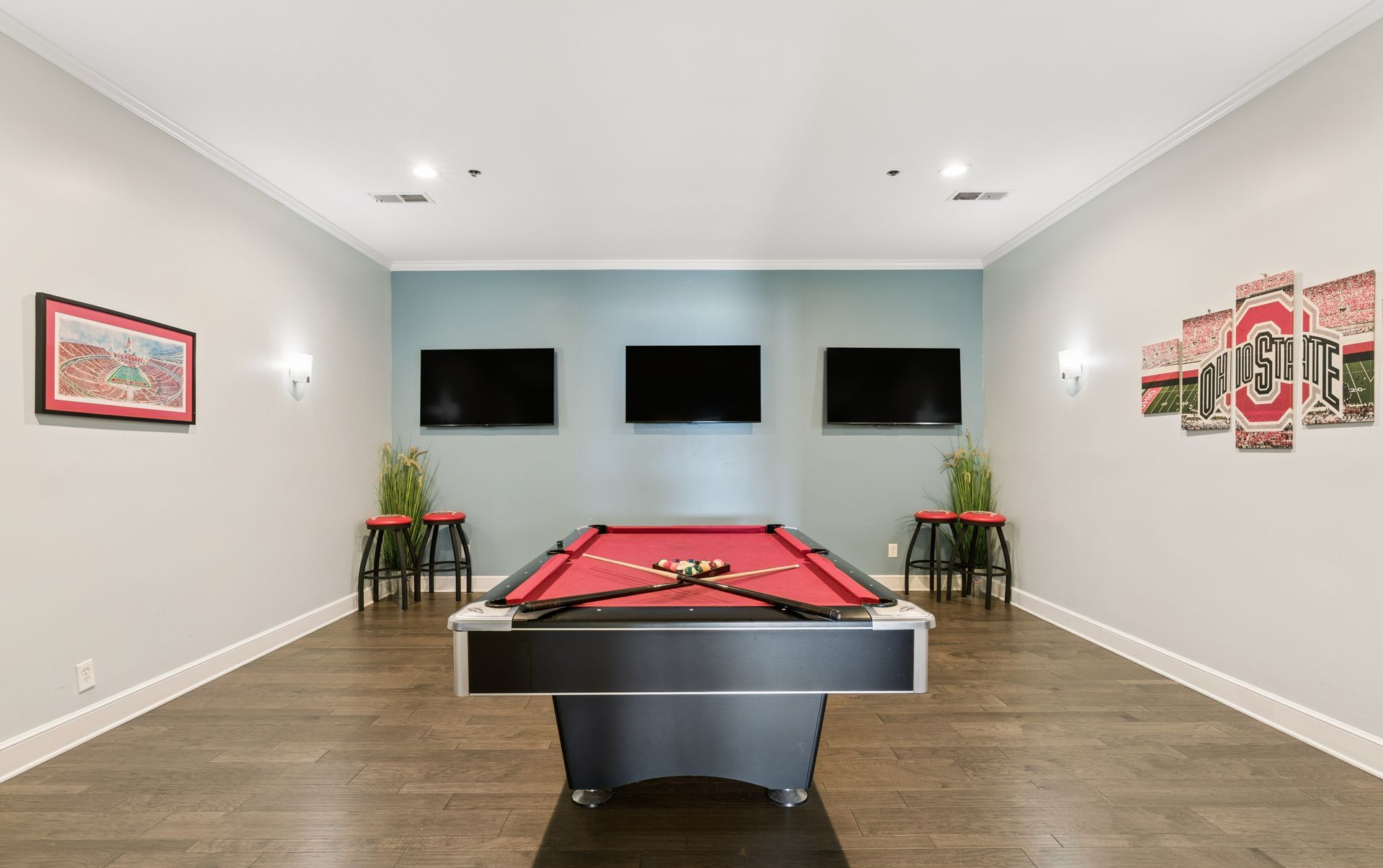 Modern game room with a pool table, wall-mounted TVs, and wall art on gray walls.