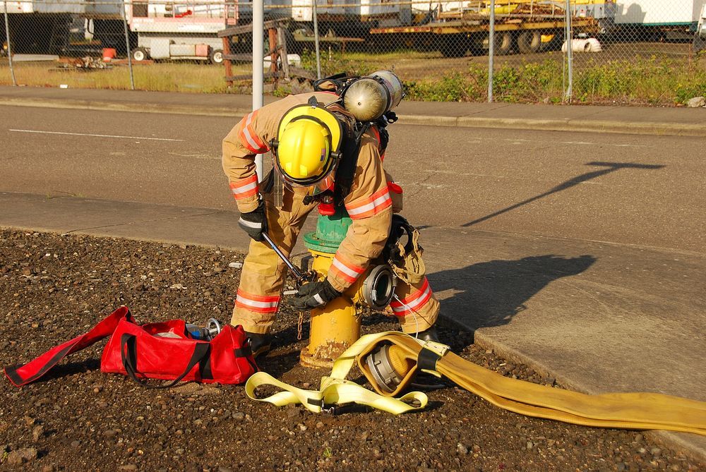 Firefighter in Full Gear Connecting a Hose to a Fire Hydrant on a Street — Industry Fire Services in Bowen, QLD