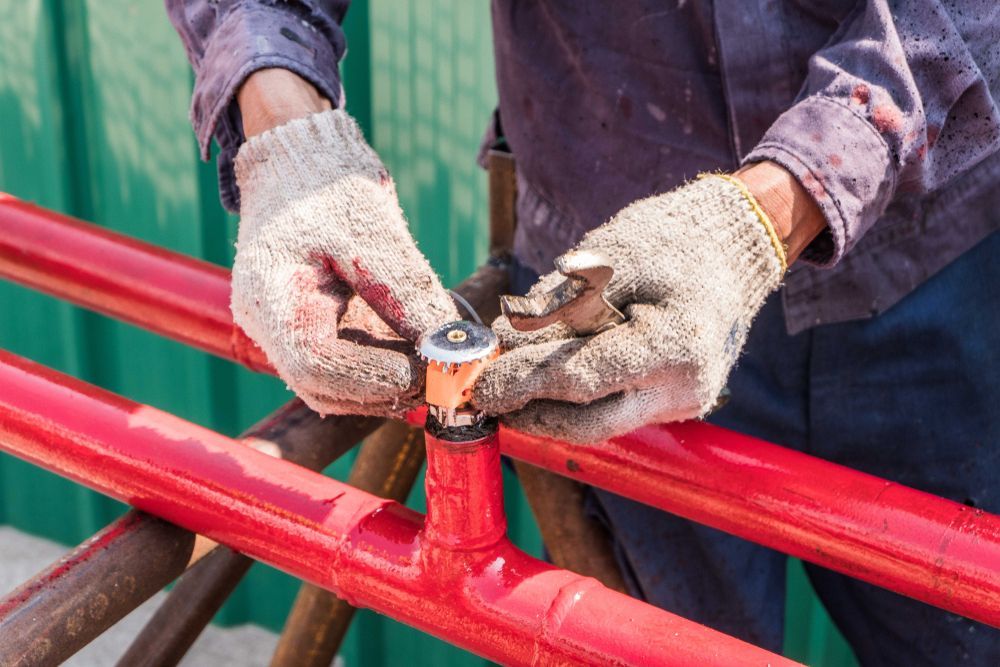 Person With Gloves Working on Red Metal Pipes — Industry Fire Services in Bowen, QLD