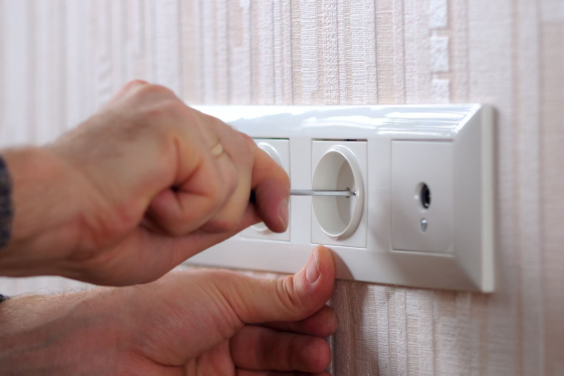 Hand Inserting a Screwdriver Into an Electrical Outlet on a White Wall Plate — Industry Fire Services in Gold Coast, QLD