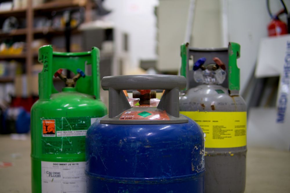 Three Different Colored Refrigerant Tanks With Valves, in a Workshop Setting — Industry Fire Services in Bowen, QLD