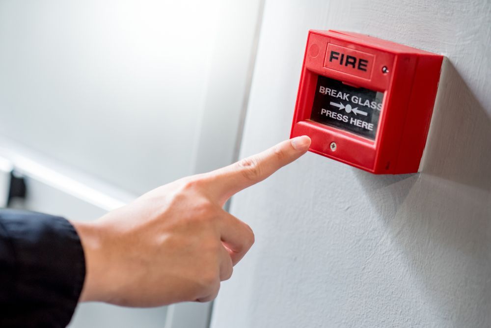 Hand Pressing a Red Fire Alarm on a White Wall — Industry Fire Services in Sunshine Coast, QLD