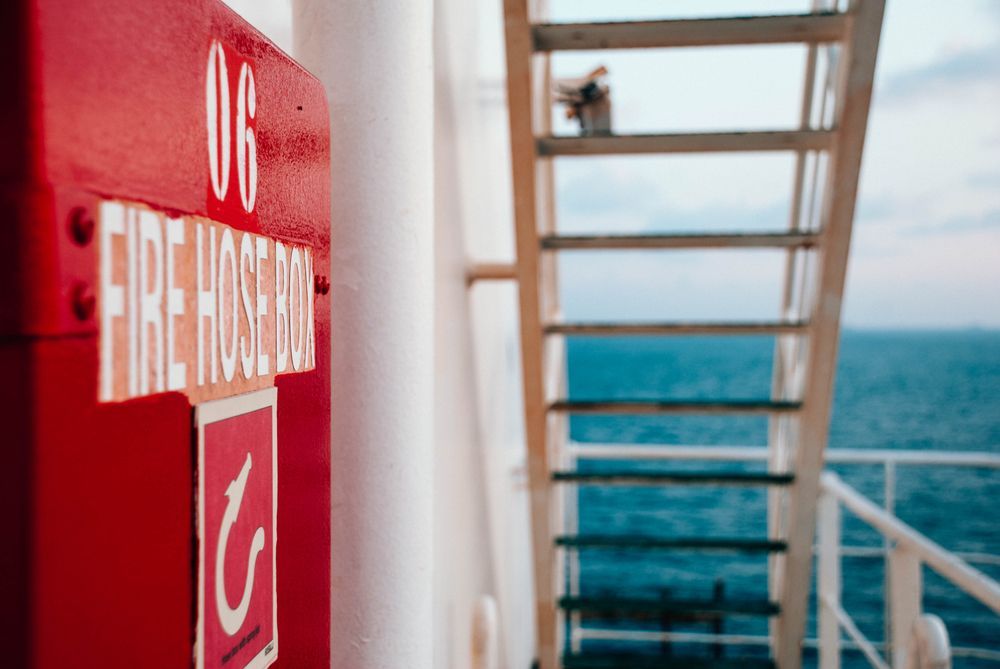 Red Fire Hose Cabinet on a Ship With a Ladder and Ocean in the Background — Industry Fire Services in Airlie Beach, QLD