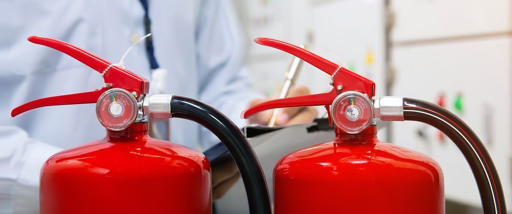 Two Red Fire Extinguishers Being Inspected, a Person Writing in the Background — Industry Fire Services in Airlie Beach, QLD