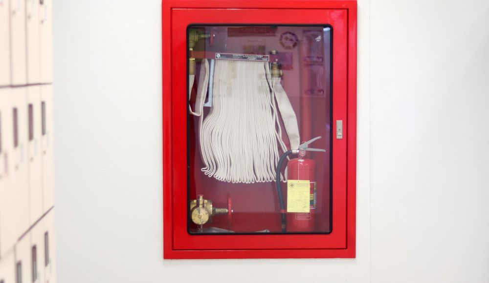 Red Fire Hose Cabinet on a White Wall Containing Fire Extinguisher — Industry Fire Services in Airlie Beach, QLD
