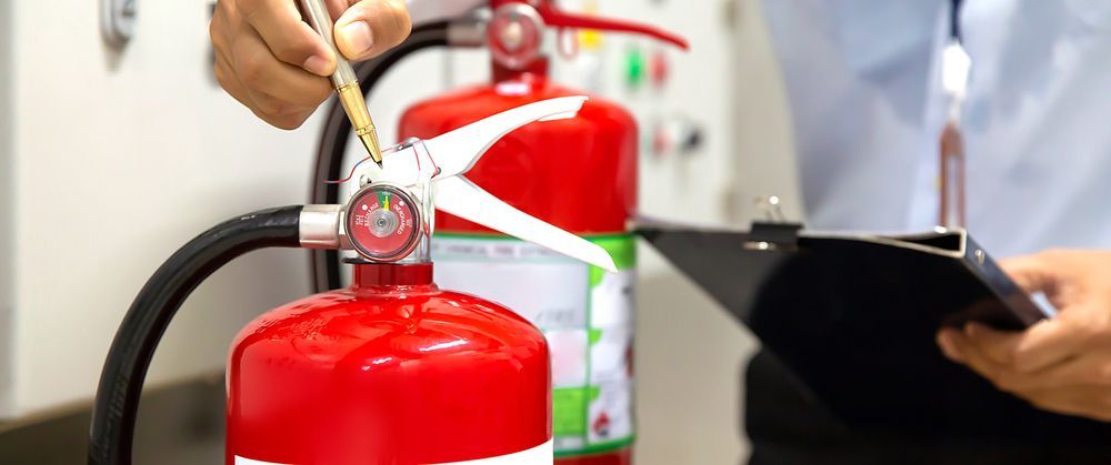 Person Inspecting a Red Fire Extinguisher With a Clipboard — Industry Fire Services in Mount Isa, QLD