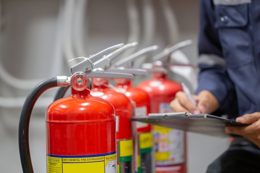 Person Inspecting Red Fire Extinguishers in a Room, Documenting Details — Industry Fire Services in Sunshine Coast, QLD
