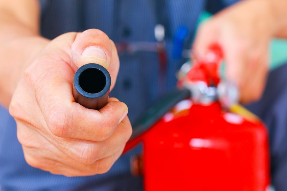 Person Holding the Nozzle of a Red Fire Extinguisher — Industry Fire Services in Sunshine Coast, QLD