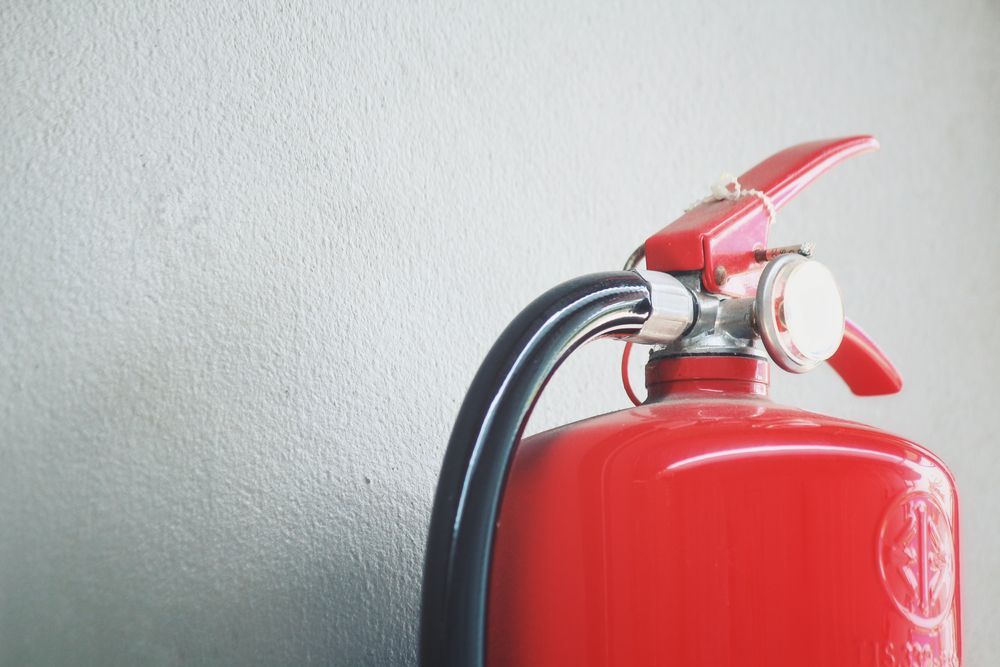 Red Fire Extinguisher Against a Gray Wall — Industry Fire Services in Toowoomba, QLD