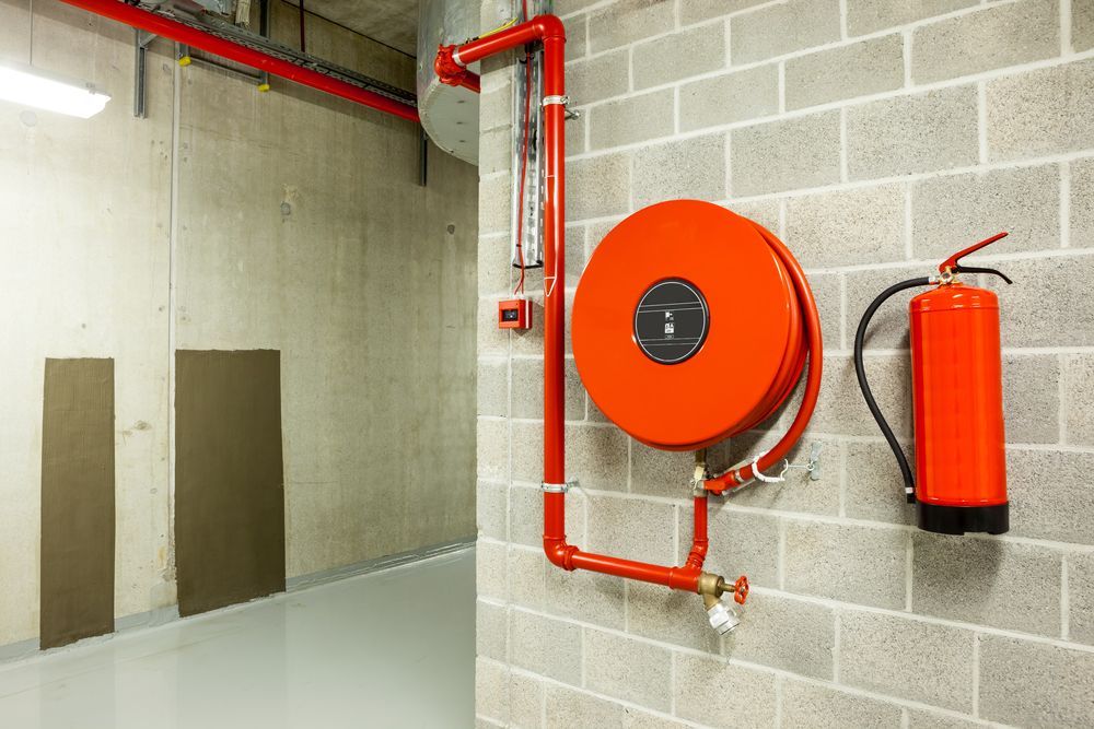 Red Fire Hose Reel and Fire Extinguisher Mounted on a Gray Cinder Block Wall — Industry Fire Services in Innisfail, QLD