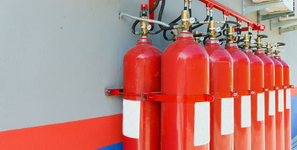 Red Fire Suppression Gas Cylinders, Mounted in a Row on a Gray Wall — Industry Fire Services in Gold Coast, QLD