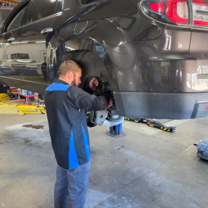 Mechanic working on the rear wheel of a black car in a garage. Wearing blue and black uniform. | Z-1 Automotive, Inc.
