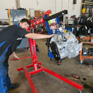 Mechanic using a red engine hoist to move a silver engine in a garage. | Z-1 Automotive, Inc.