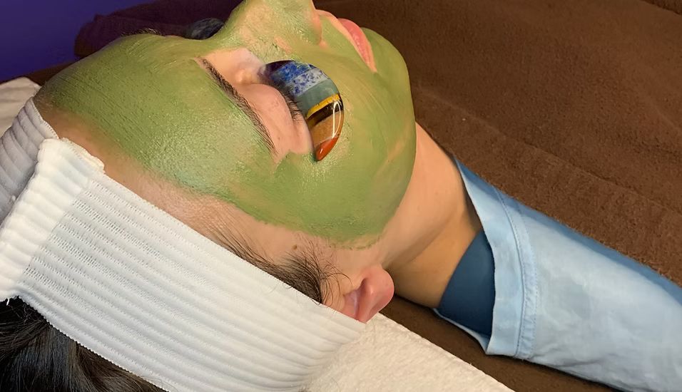 A person is laying on a bed with a green mask on their face.