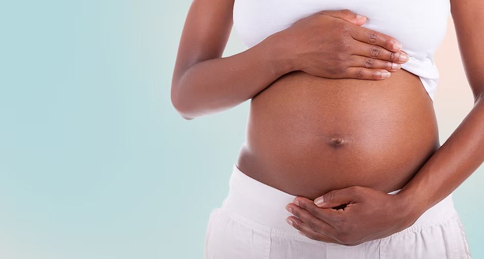 A pregnant woman is holding her belly with her hands.