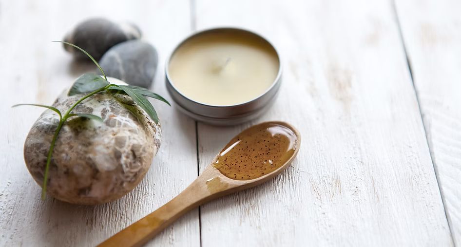 A wooden spoon filled with liquid next to a candle and a rock on a wooden table.