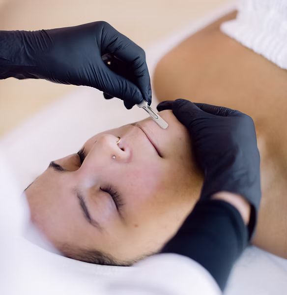 A person wearing black gloves is using a razor to shave a woman 's face
