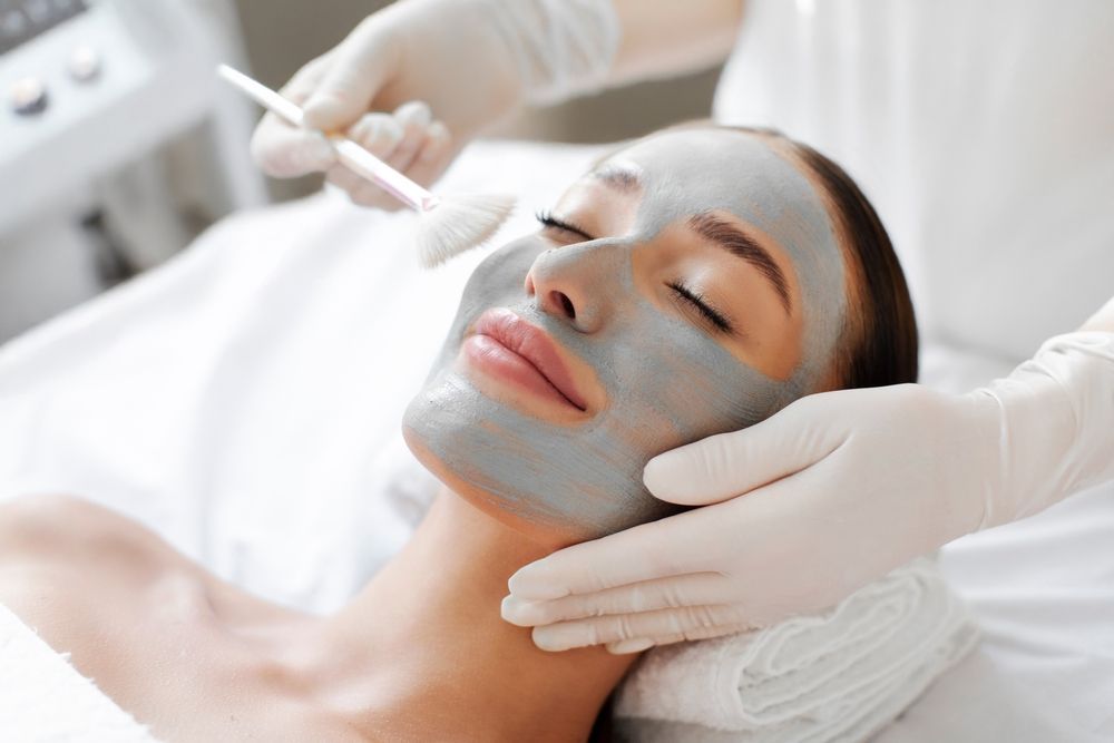 Woman with clay facial mask receiving spa treatment.