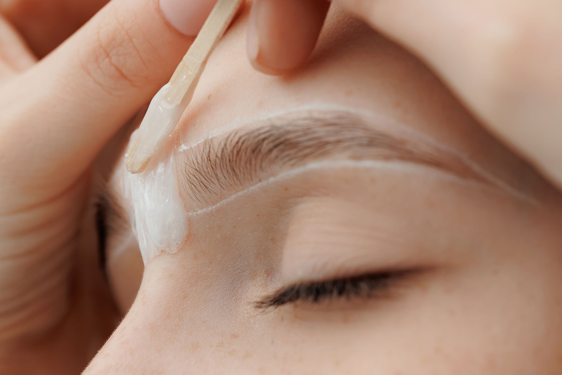 A woman is getting her eyebrows waxed by a makeup artist.