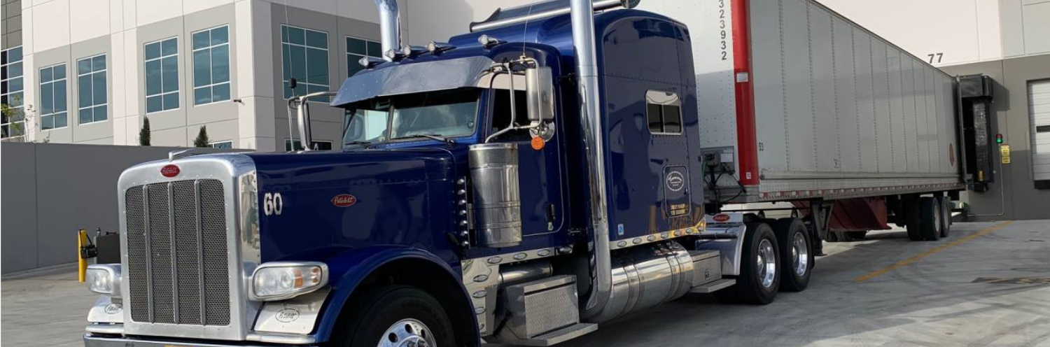 Blue semi-truck with a silver trailer parked beside a building