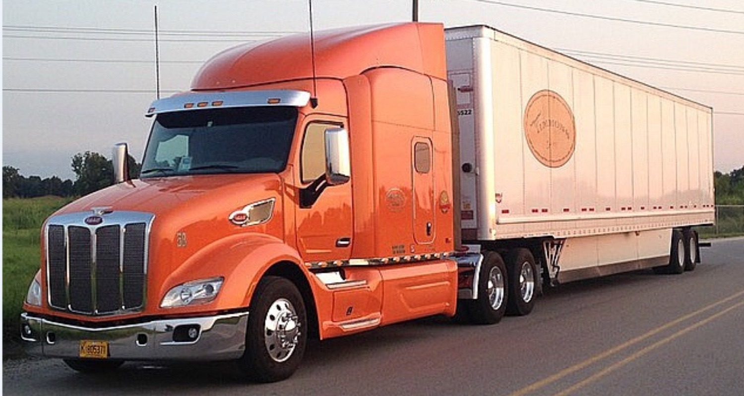 Orange semi-truck hauling a white trailer on a highway