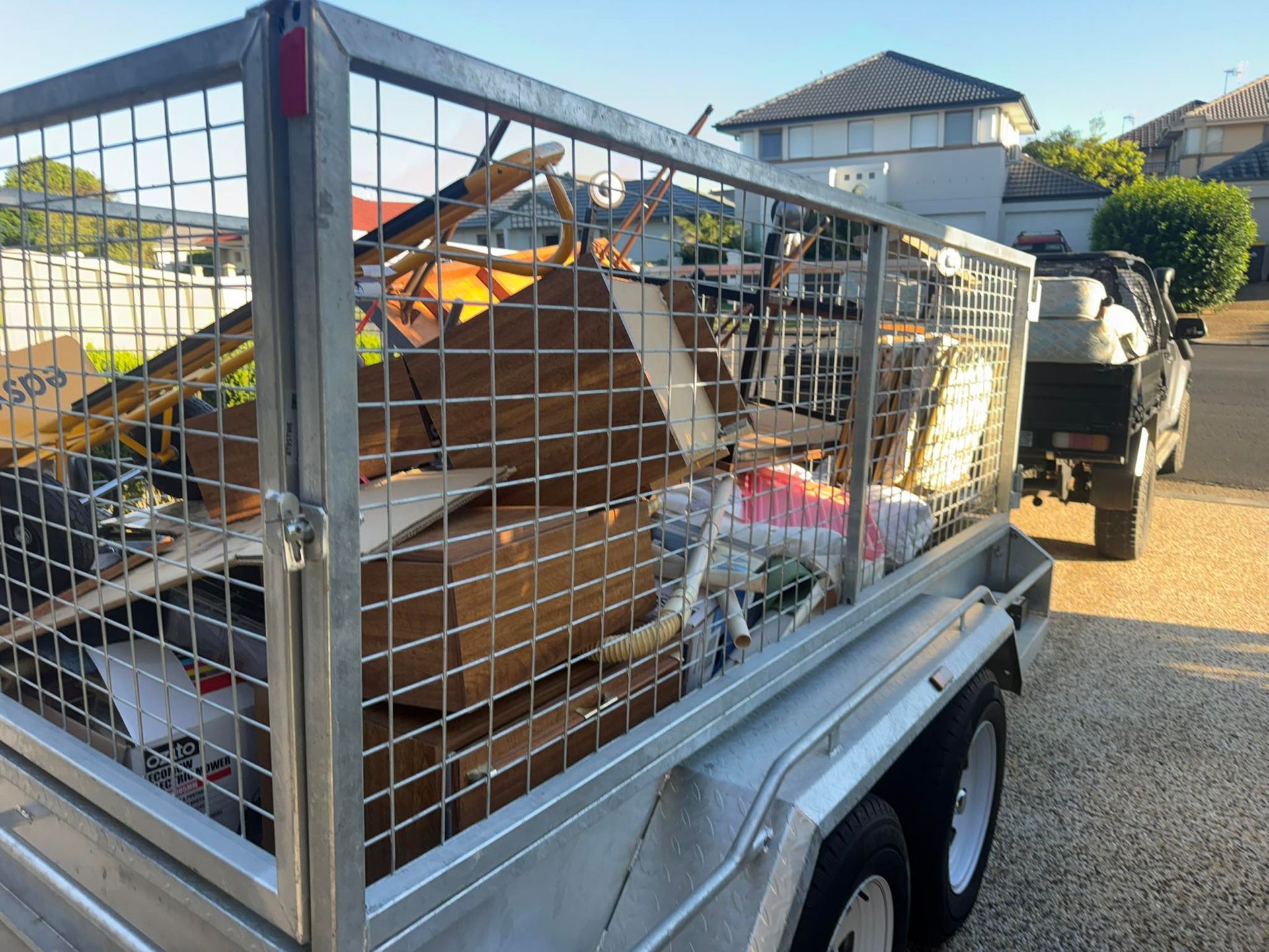 A utility trailer filled with cardboard boxes, scrap wood, and miscellaneous items parked on a residential driveway.