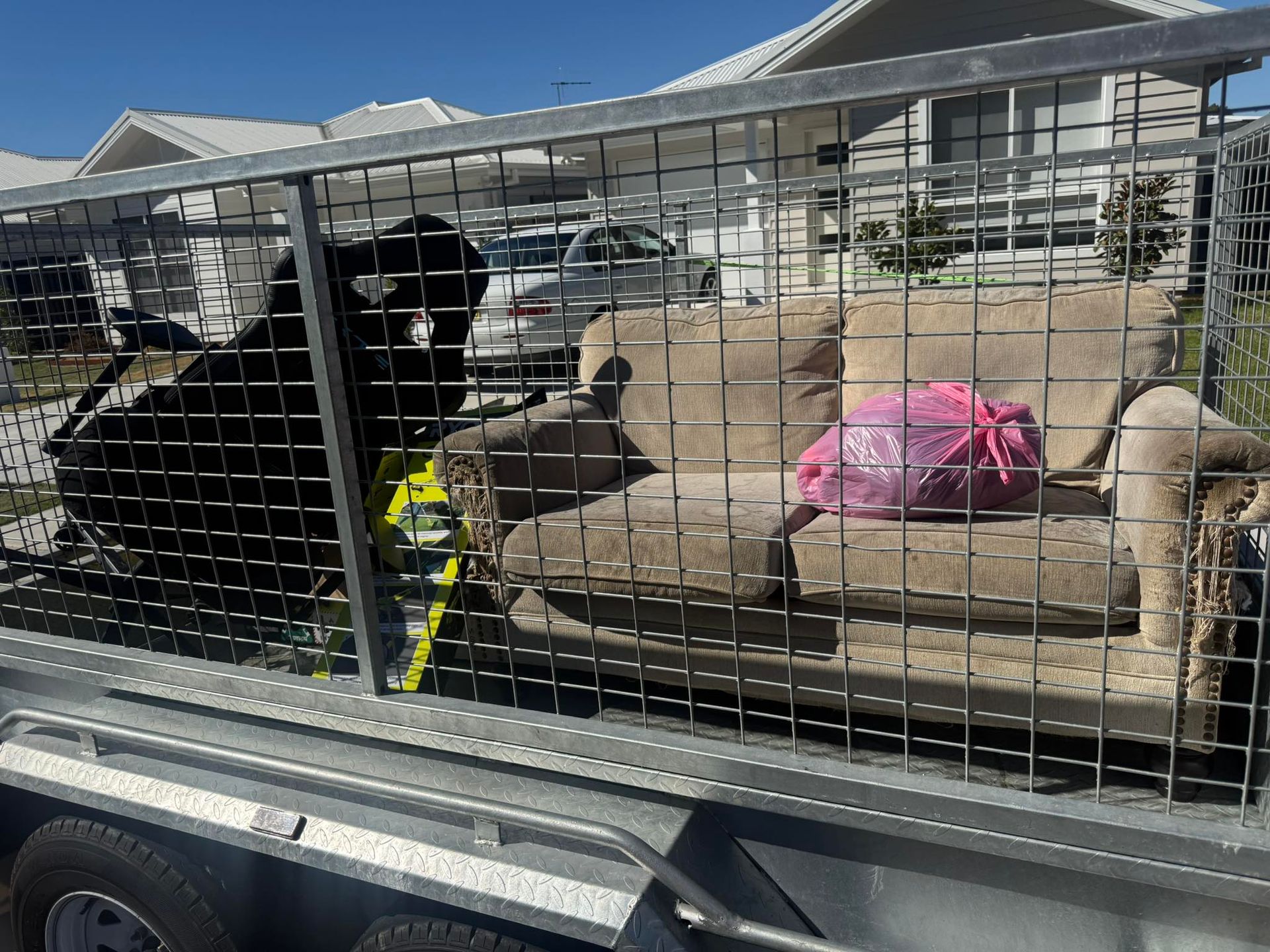 A tan couch and a pink bag sitting inside a caged metal trailer — Smiley Rubbish Removal In Lake Cathie, NSW