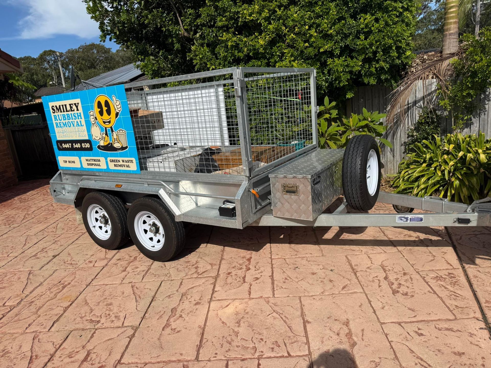 A Dual-axle Metal Utility Trailer With a Cage, a Storage Box, and Branding — Smiley Rubbish Removal In Wauchope, NSW