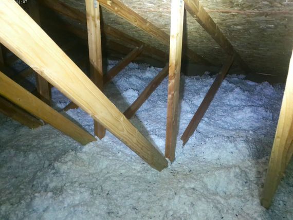 Attic space with wooden beams and white insulation.