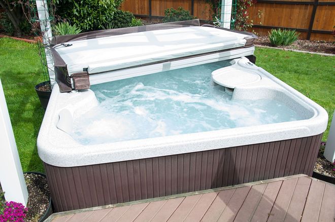 Hot tub in back yard with water bubbling and the lid half off, ready to be enjoyed in the outdoors.