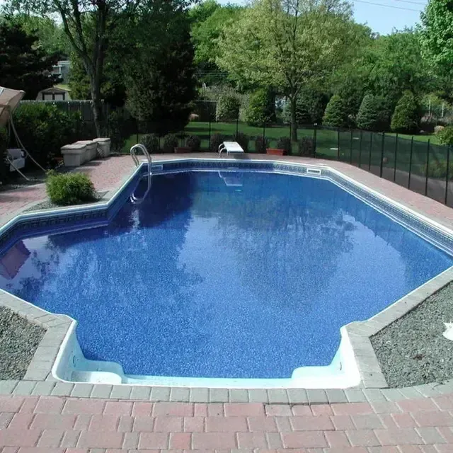 Backyard swimming pool with blue water, brick patio, and trees in the background