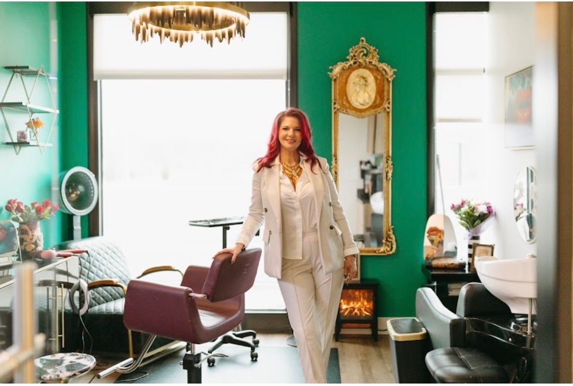 Woman standing in a bright vintage salon with turquoise walls, a gold mirror, and styling chairs