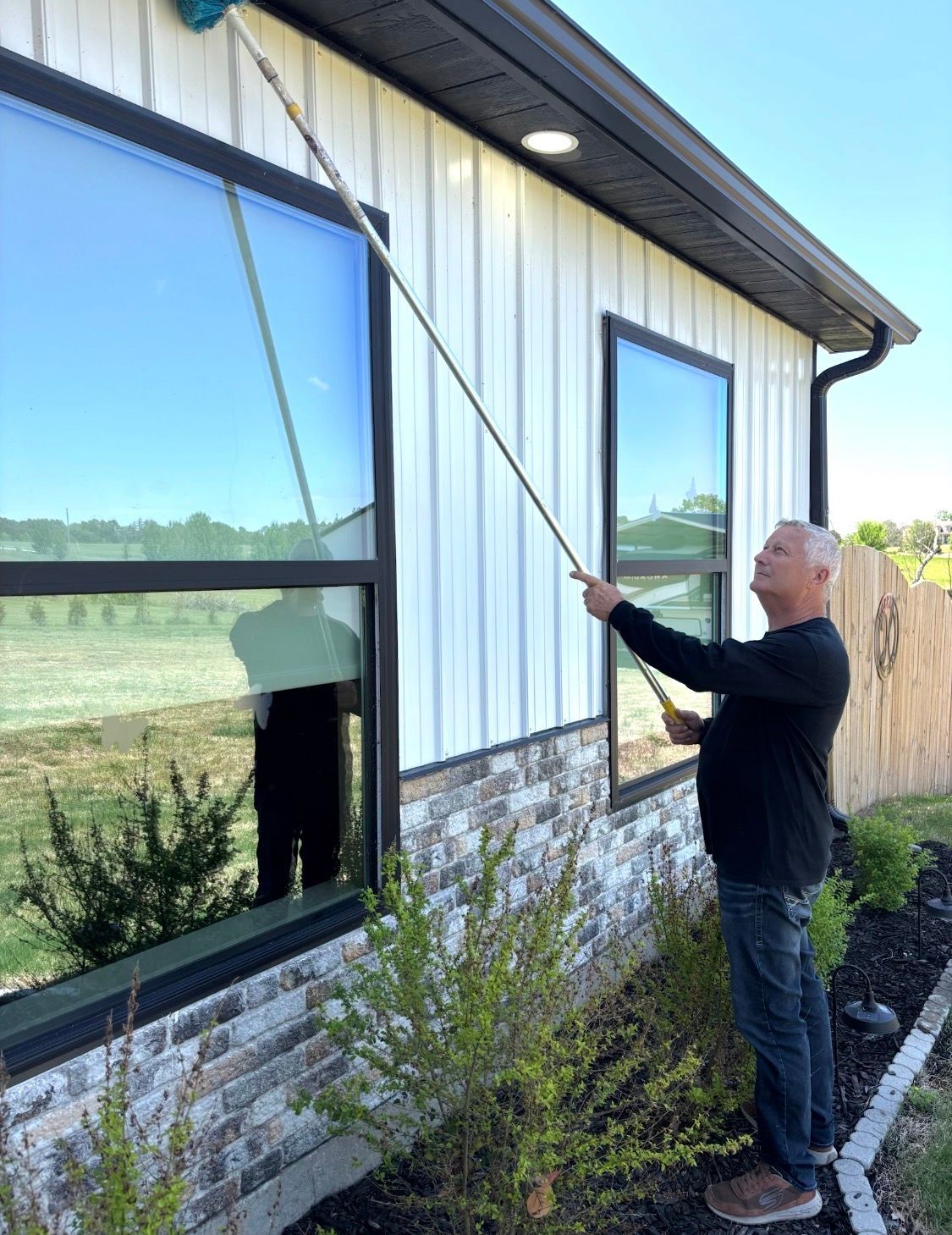 Man using a long pole to open an upper window beside a white house