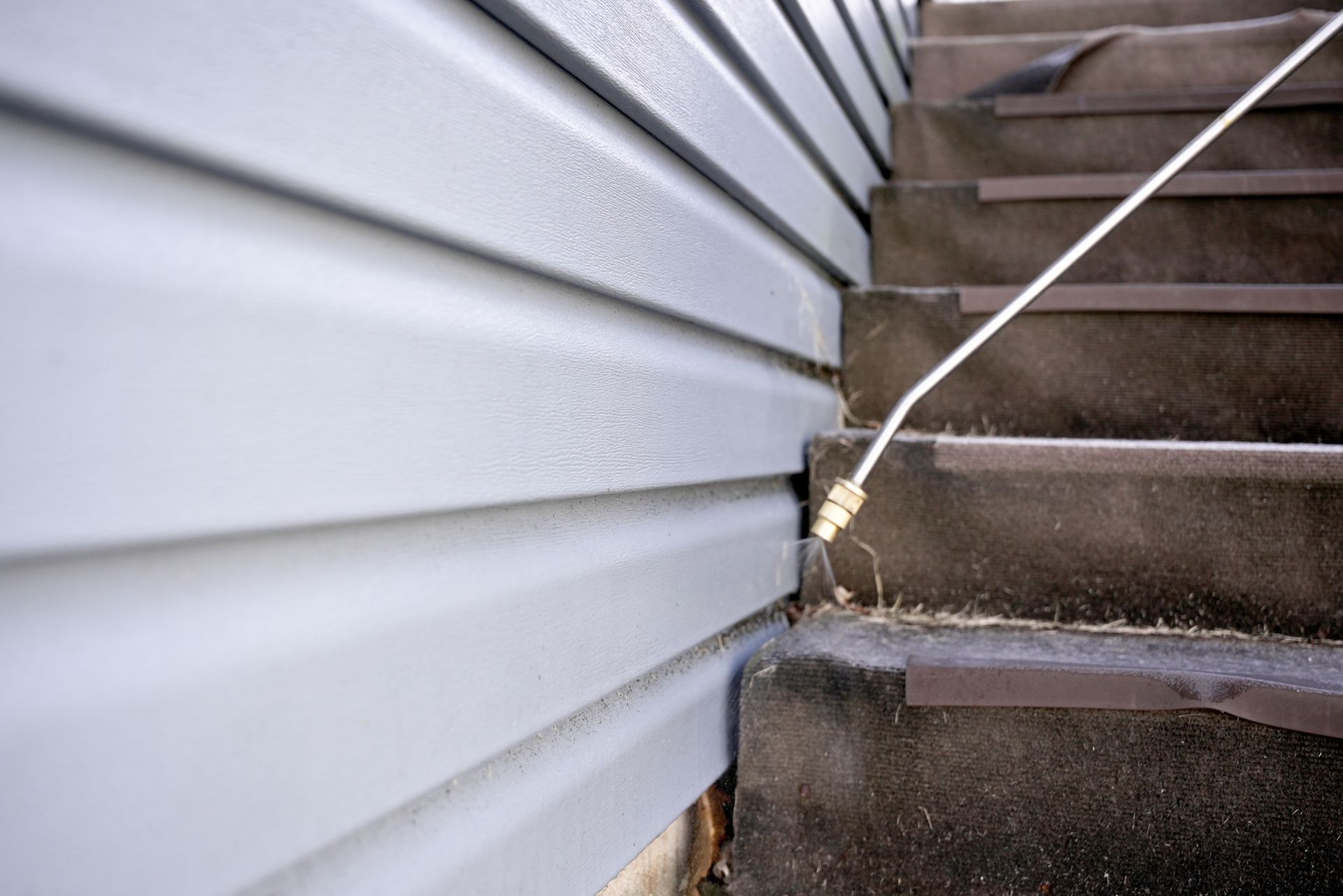 Close-up of house siding meeting outdoor stairs, with a white cable running along the corner.