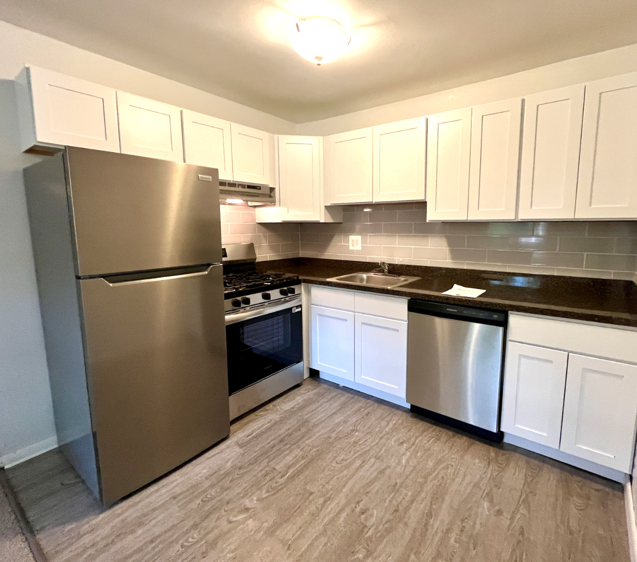 Modern white kitchen with stainless steel appliances, dark countertops, and light wood flooring