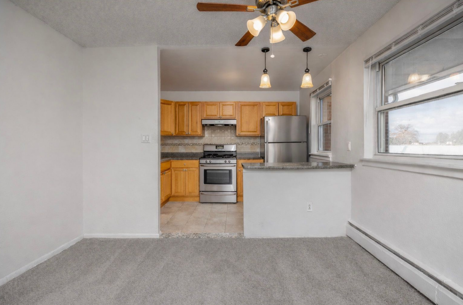 A carpeted dining area opening to a kitchen with light wood cabinets, stainless steel appliances, and a tiled floor.
