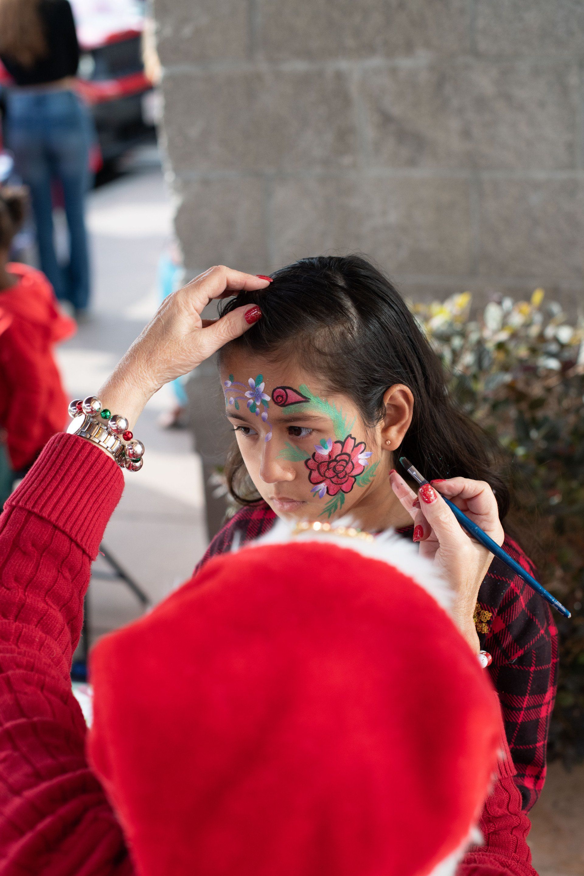 A little girl is getting her face painted by santa claus.