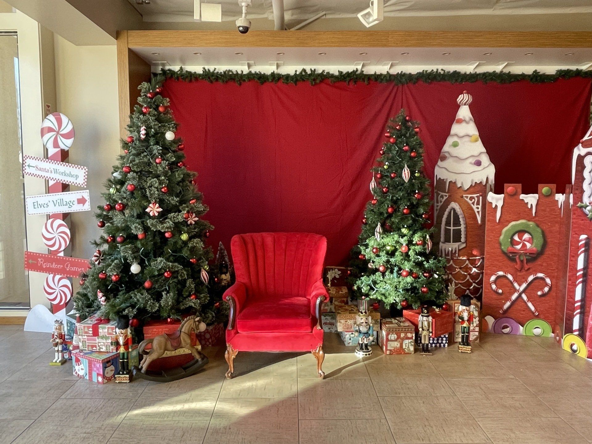 A red chair is sitting in front of a christmas tree and gingerbread house.