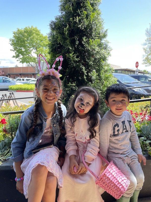 Three children are sitting next to each other in front of a tree.
