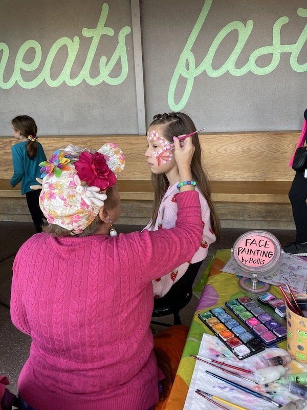 A girl is getting her face painted in front of a sign that says greats fast