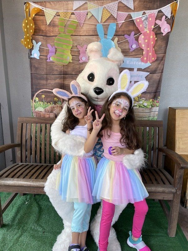 Two little girls are posing for a picture with an easter bunny mascot.