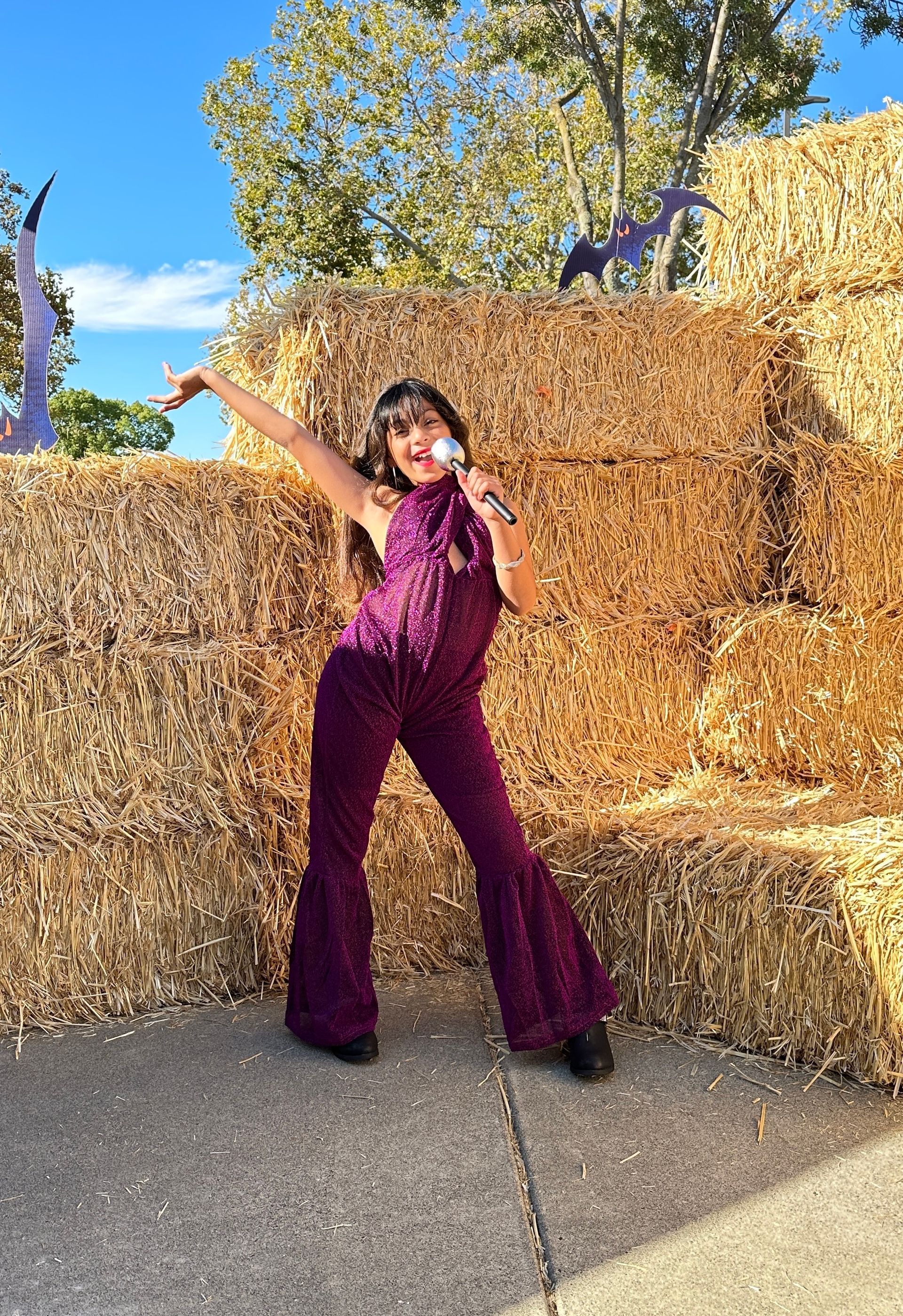 A woman in a purple jumpsuit is standing in front of a pile of hay.