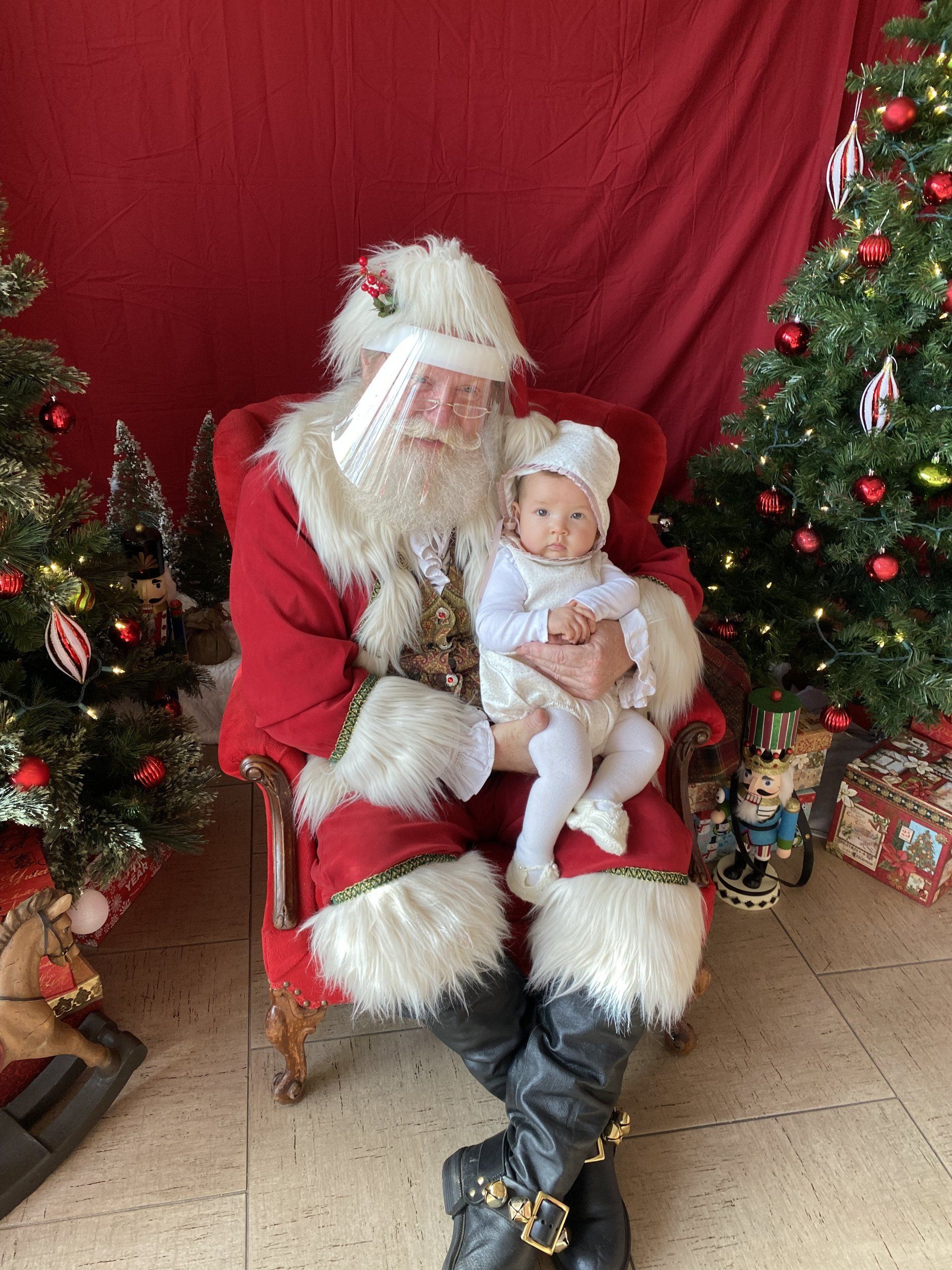 A man dressed as santa claus is holding a baby in front of a christmas tree.