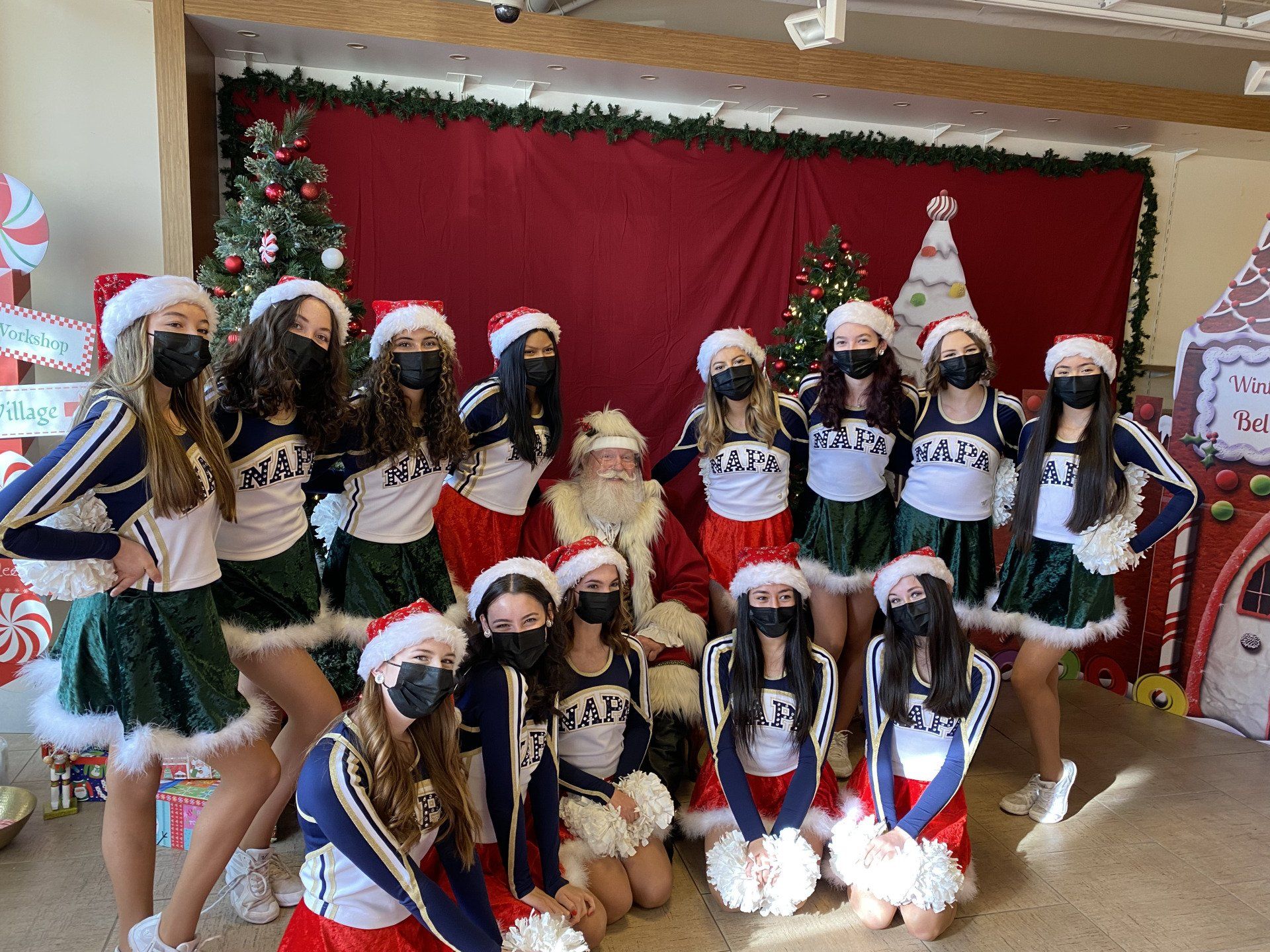 A group of cheerleaders are posing for a picture with santa claus.